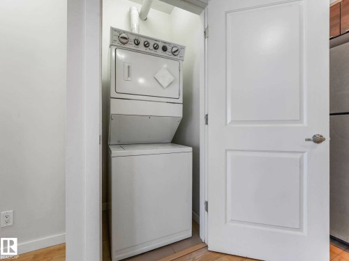 In-unit laundry closet with a stacked washer and dryer, adjacent to a paneled interior door with brushed nickel hardware - 406 9519 160 Avenue, Edmonton, AB 