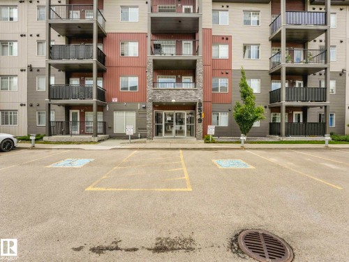 Multi-story apartment building featuring balconies with black railings, a stone facade entrance, and a paved parking area - 406 9519 160 Avenue, Edmonton, AB 