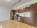 Modern kitchen featuring wood-finish cabinetry, stainless steel appliances, white countertop, and a textured tile backsplash - 406 9519 160 Avenue, Edmonton, AB 