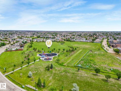 Expansive green space featuring a playground area, paved walking paths, scattered trees, and surrounding residential development - 406 9519 160 Avenue, Edmonton, AB 