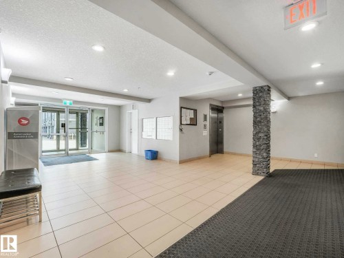 Lobby area featuring light-toned tile flooring, a stone-clad structural column, recessed lighting, and a stainless steel elevator - 406 9519 160 Avenue, Edmonton, AB 