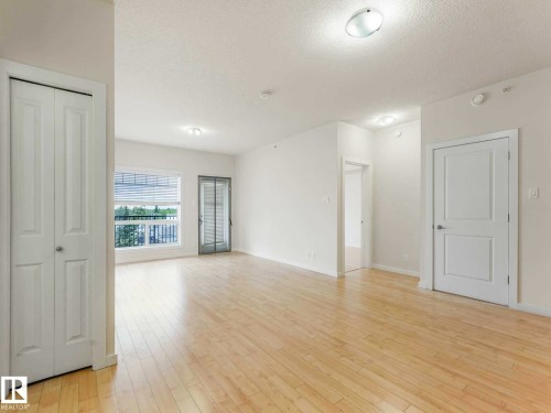 Bright interior space featuring wood-finish flooring, white walls, and a large window with horizontal blinds - 406 9519 160 Avenue, Edmonton, AB 