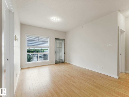 Spacious room featuring light wood-finish flooring, white walls, and a large window with horizontal blinds - 406 9519 160 Avenue, Edmonton, AB 