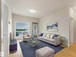 Living area featuring light wood-finish flooring, white walls, and a large window with horizontal blinds - 