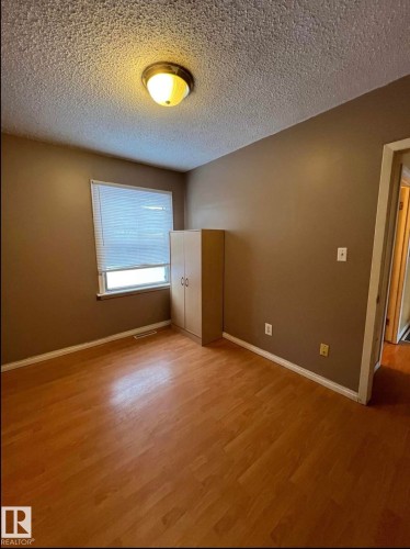 Room featuring wood-finish flooring, a window with horizontal blinds, and a neutral-toned ceiling light fixture - 9209 150 Street, Edmonton, AB 