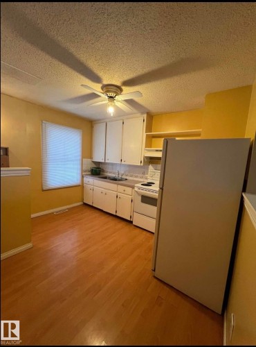 Kitchen featuring white cabinetry, a double basin sink, and wood-finish flooring - 9209 150 Street, Edmonton, AB 