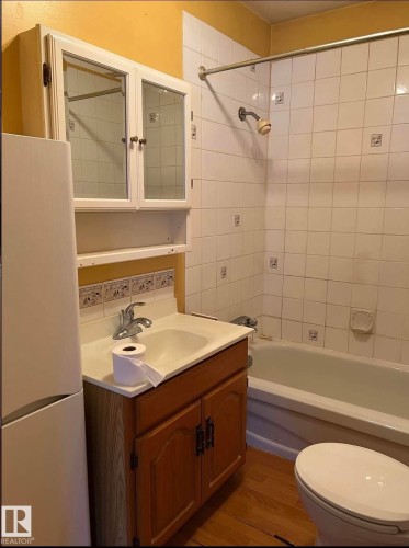 Bathroom featuring a wood-finish vanity with an integrated sink, white tiled shower and tub surround, and a wall-mounted medicine cabinet - 9209 150 Street, Edmonton, AB 