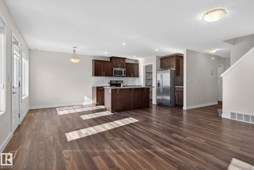 Spacious interior featuring wood-finish flooring, a kitchen island with built-in cabinetry, stainless steel appliances, and multiple windows - 5306 67 Street E, Beaumont, AB 