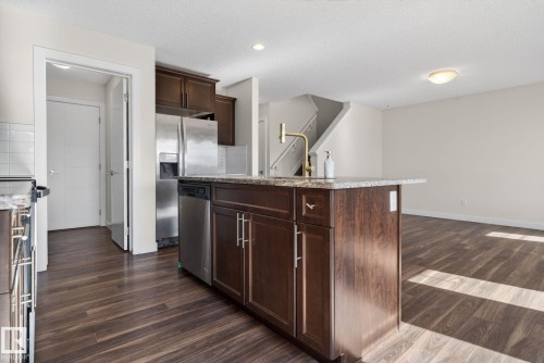 Kitchen island featuring a granite-style countertop, gold-tone faucet, and dark wood cabinetry - 5306 67 Street E, Beaumont, AB 