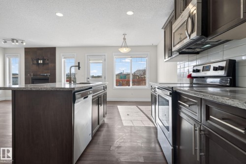Open-concept kitchen featuring dark wood cabinetry, stainless steel appliances, granite countertops, and a subway tile backsplash - 5306 67 Street E, Beaumont, AB 
