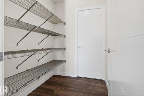 Interior closet featuring multi-tiered wire shelving, wood-finish flooring, and a modern white panel door with a chrome handle - 5306 67 Street E, Beaumont, AB 