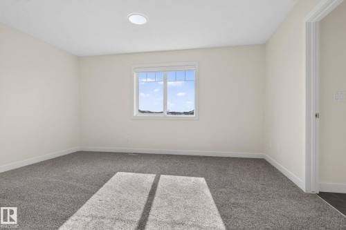 Carpeted interior room featuring a large window, a circular flush-mount ceiling light, white baseboards, and a doorway with white trim - 5306 67 Street E, Beaumont, AB 