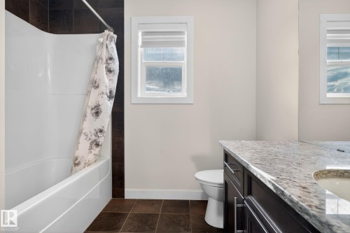 Bathroom featuring a white tub-shower combination with dark tile surround, a white window, a dark wood-finish vanity with a light-colored countertop, and dark floor tiles - 5306 67 Street E, Beaumont, AB 