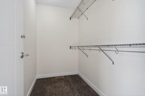 Walk-in closet with wire shelving system, hanging rods, light-colored walls, and dark carpet flooring - 5306 67 Street E, Beaumont, AB 