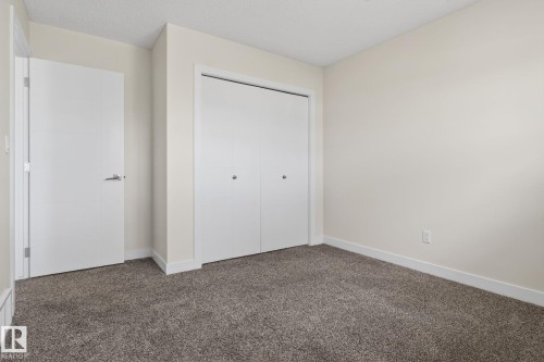 Neutral toned room featuring plush gray carpeting, white baseboards, a flat white door with a contemporary handle, and a white bi-fold closet door - 5306 67 Street E, Beaumont, AB 