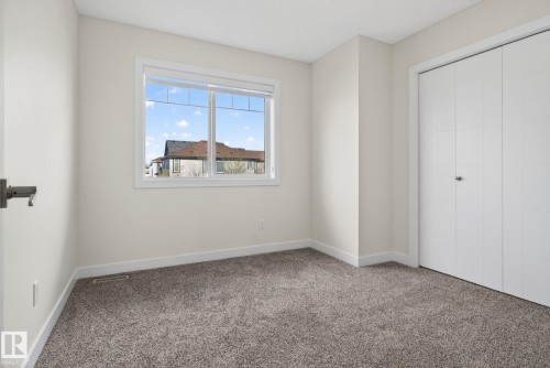 Spacious room featuring neutral paint, gray speckled carpet, a large window, white baseboards, and a bi-fold closet - 5306 67 Street E, Beaumont, AB 