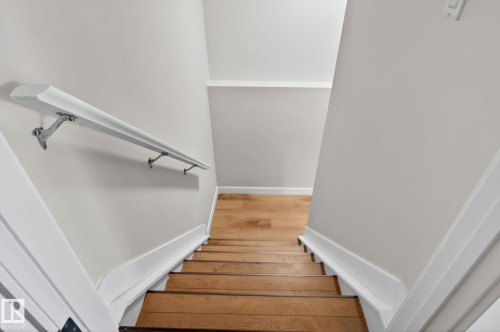 Hardwood staircase featuring a white handrail with metal brackets, white baseboards, and light-colored wall paint - 5306 67 Street E, Beaumont, AB 
