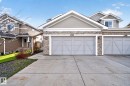 Modern townhome facade featuring light gray siding with stone accents, a two-car garage with decorative paneling, and a concrete driveway - 5306 67 Street E, Beaumont, AB 