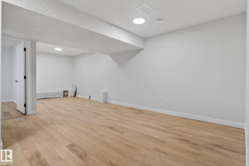 Spacious room featuring light wood-finish flooring, recessed lighting, and crisp white walls - 5306 67 Street E, Beaumont, AB 