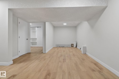 Spacious room featuring light wood-finish flooring, white baseboards, and neutral wall paint - 5306 67 Street E, Beaumont, AB 
