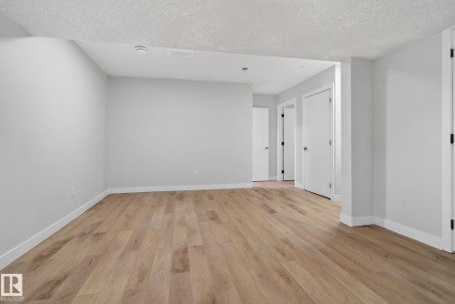 Spacious room featuring light wood-finish flooring, white baseboards, light gray walls, and multiple white doors with dark hardware - 5306 67 Street E, Beaumont, AB 