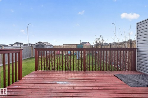 Expansive backyard featuring a red-stained wooden deck, lush green lawn, and full perimeter wood fencing - 5306 67 Street E, Beaumont, AB 