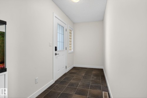 Entryway featuring dark square tile flooring, a white paneled door with glass inserts, and a sidelight with horizontal blinds - 5306 67 Street E, Beaumont, AB 
