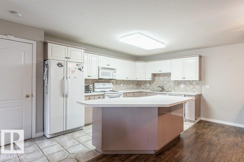 Kitchen featuring a spacious island, white cabinetry, a built-in microwave, and a tile backsplash - 101 10421 42 Avenue, Edmonton, AB 