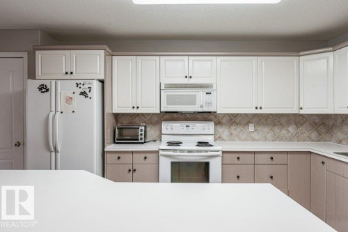 Kitchen featuring white upper cabinetry, light wood-finish lower cabinetry, and a patterned tile backsplash - 101 10421 42 Avenue, Edmonton, AB 