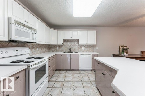 Kitchen featuring white upper cabinetry, two-tone lower cabinetry, white countertops, and a patterned tile backsplash - 101 10421 42 Avenue, Edmonton, AB 