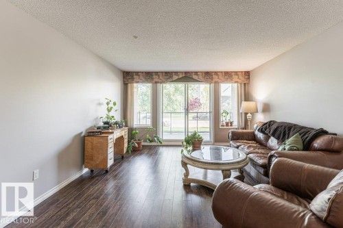 Living room featuring wood-finish flooring, light-toned walls, and a textured ceiling - 101 10421 42 Avenue, Edmonton, AB 