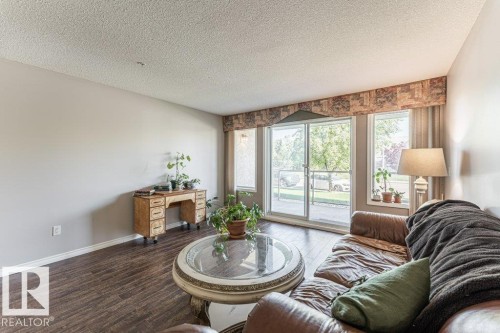 Spacious living area featuring dark wood-finish flooring and light-toned walls - 101 10421 42 Avenue, Edmonton, AB 