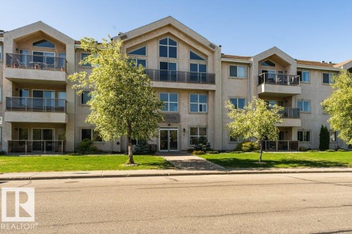 Multi-story residential building featuring stucco exterior, multiple balconies with glass railings, large windows, and gabled roof accents - 101 10421 42 Avenue, Edmonton, AB 