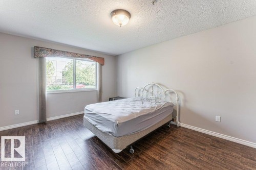 Bedroom featuring wood-finish flooring, a large window, and light-colored walls - 101 10421 42 Avenue, Edmonton, AB 
