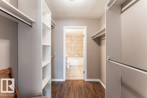 Walk-in closet with integrated shelving, multiple hanging rods, and wood-finish flooring - 101 10421 42 Avenue, Edmonton, AB 