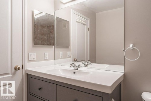 Vanity featuring a white countertop with integrated sink, chrome faucet, and gray cabinetry with black hardware - 101 10421 42 Avenue, Edmonton, AB 