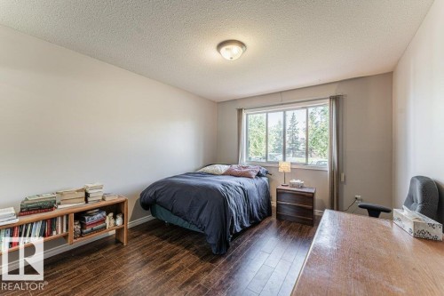 Spacious room featuring wood-finish flooring, a large window, neutral wall tones, and a ceiling-mounted light fixture - 101 10421 42 Avenue, Edmonton, AB 