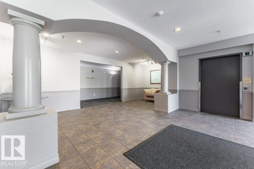 Building lobby featuring tiled flooring, architectural columns, an arched doorway, recessed lighting, and paneling along the walls - 101 10421 42 Avenue, Edmonton, AB 