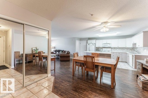 Open-concept living area featuring wood-finish flooring, a kitchen with white cabinetry and appliances, a dining area, and mirrored closet doors - 101 10421 42 Avenue, Edmonton, AB 