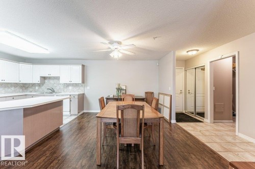 Open-concept living area featuring wood-finish flooring, a kitchen island with seating, white shaker-style cabinetry, and a ceiling fan - 101 10421 42 Avenue, Edmonton, AB 
