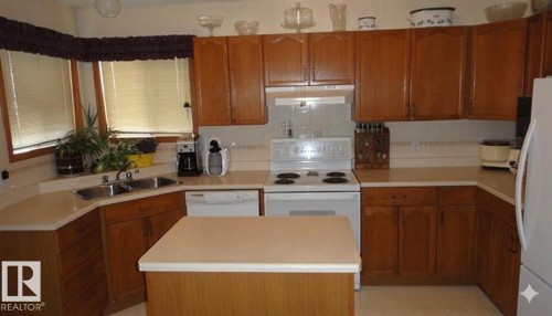 Kitchen featuring ample wood cabinetry, a central island with a solid surface countertop, a double basin stainless steel sink, a bay window, and a tile backsplash - 1188 Joyce Road Nw, Edmonton, AB 
