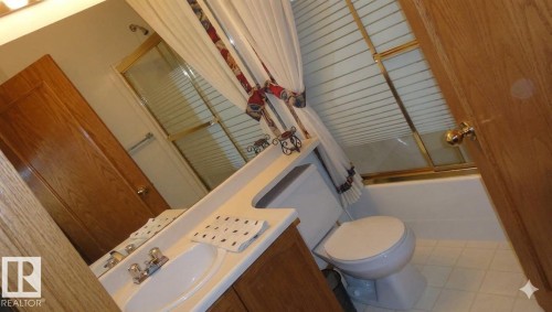 Bathroom featuring a vanity with a drop-in sink, gold-toned fixtures, a mirrored wall, and a bathtub with a gold-framed sliding glass enclosure - 1188 Joyce Road Nw, Edmonton, AB 
