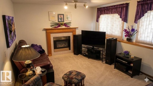 Carpeted living area featuring a fireplace with a wood mantel and tile surround - 1188 Joyce Road Nw, Edmonton, AB 