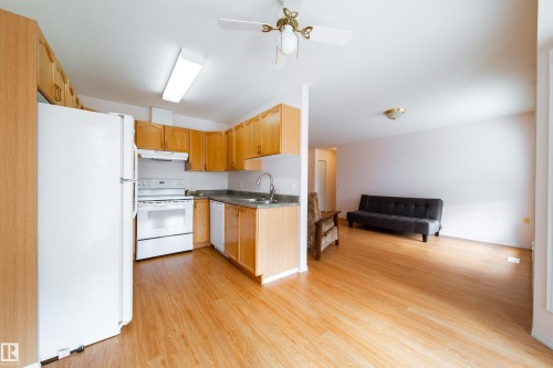 Open-concept kitchen featuring light wood-finish cabinetry, white appliances, and a stainless steel sink - 120 13320 124 Street Nw, Edmonton, AB 