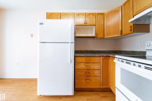 Kitchen featuring wood-finish cabinetry, solid surface countertops, white refrigerator, and an electric range - 120 13320 124 Street Nw, Edmonton, AB 