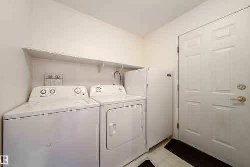 Laundry area featuring a top-load washing machine, front-load dryer, and wall-mounted shelving - 120 13320 124 Street Nw, Edmonton, AB 