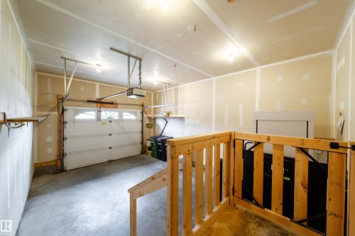 Attached garage featuring a white sectional overhead door with upper window inserts, an automatic garage door opener, and exposed drywall - 120 13320 124 Street Nw, Edmonton, AB 