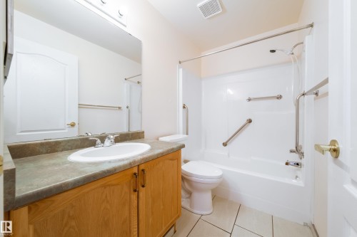 Bathroom featuring a wood-finish vanity with an integrated basin, a stone-finish countertop, and a large wall-mounted mirror - 120 13320 124 Street Nw, Edmonton, AB 
