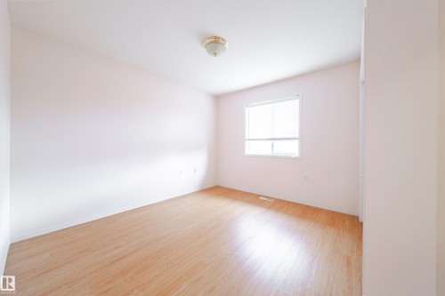 Bright interior space featuring wood-finish flooring, light-toned walls, a white-framed window with horizontal blinds, and a ceiling-mounted light fixture - 120 13320 124 Street Nw, Edmonton, AB 