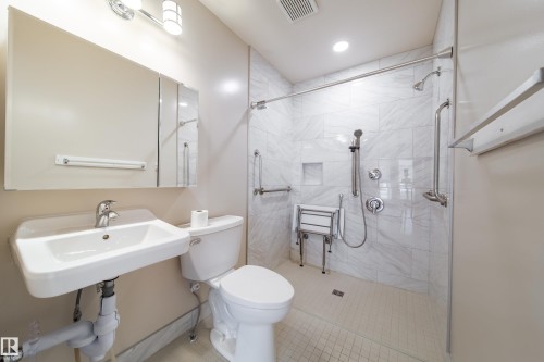 Walk-in shower with white tile surround and integrated shelving, featuring a handheld showerhead and grab bars - 120 13320 124 Street Nw, Edmonton, AB 